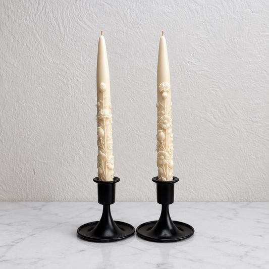 Ivory wildflower taper candles in black holders on marble.