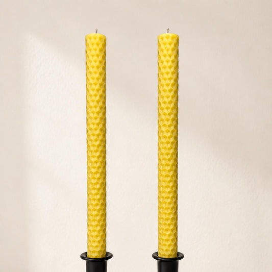 Pair of golden honeycomb-textured beeswax taper candles in black holders.