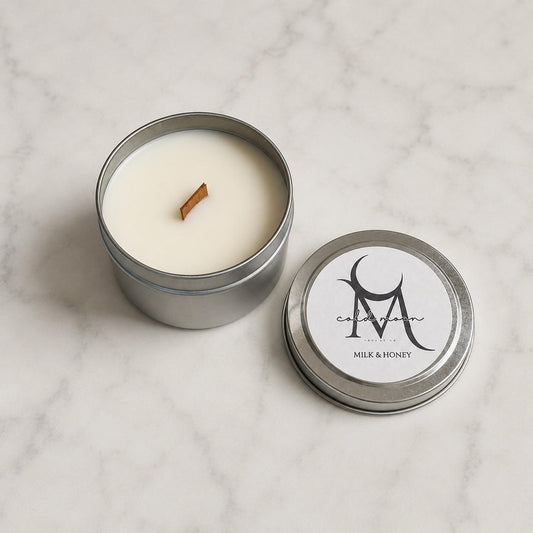 Open Milk & Honey wood-wick candle in a silver tin beside its labeled lid on marble.