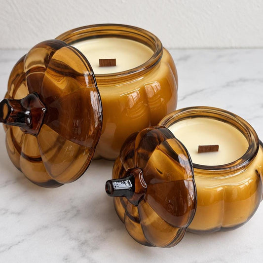 Two Pumpkin Bourbon Cake candles in amber glass pumpkin jars with lids beside them.