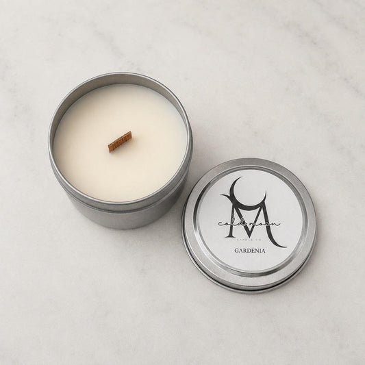 Open Gardenia wood-wick candle in a silver tin beside its labeled lid on marble.