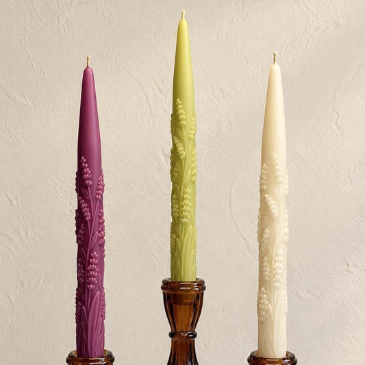 Purple, pale green, and ivory lavender sprig taper candles in amber glass holders.